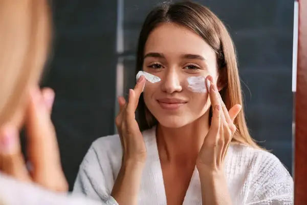 Kobieta w białym szlafroku nakłada kremy spf na twarz, dbając o ochronę skóry przed słońcem.