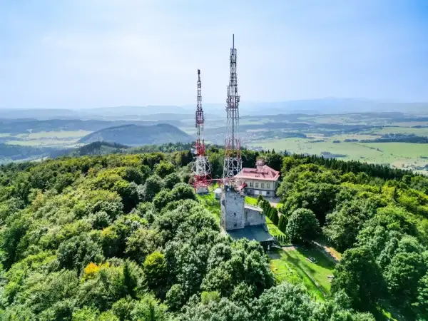 Wieże telekomunikacyjne na zalesionym szczycie Chełmiec. W tle rozległa panorama krajobrazu.