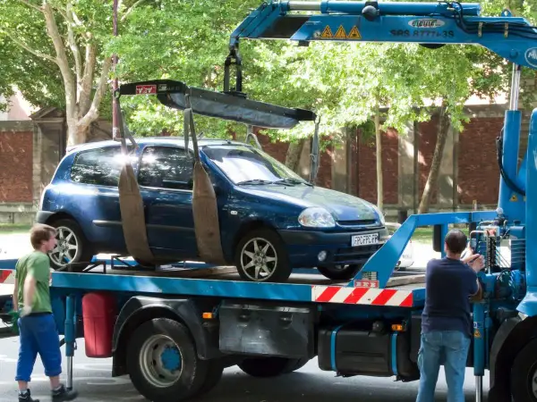Une dépanneuse charge une voiture bleue. Si vous vous demandez comment savoir si ma voiture est à la fourrière, regardez si elle disparaît de là où vous l'avez garée.