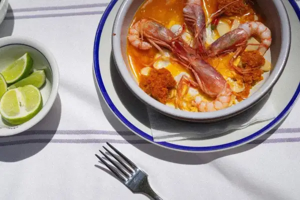 Un plato de gambas en salsa, preparado por un chef del mar, con gajos de lima al lado.