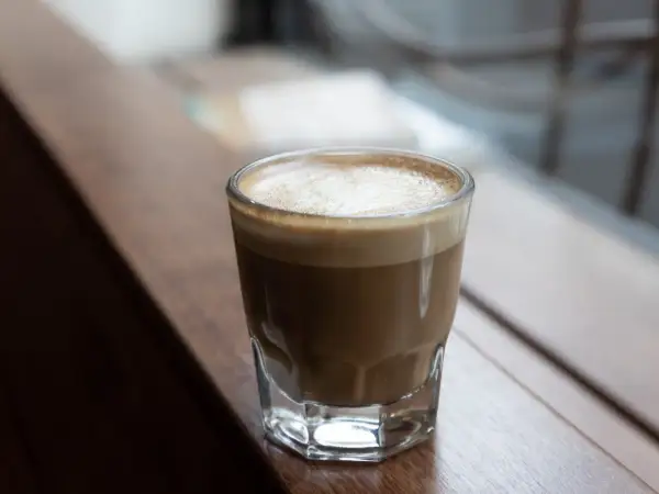 En perfekt cortado macchiato med krämigt skum, serverad i ett glas på en träyta.