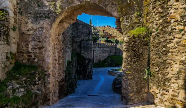 Un pasaje de piedra antigua nos lleva a descubrir lugares secretos de la Sierra de Madrid, con un camino empedrado y murallas que evocan historia.