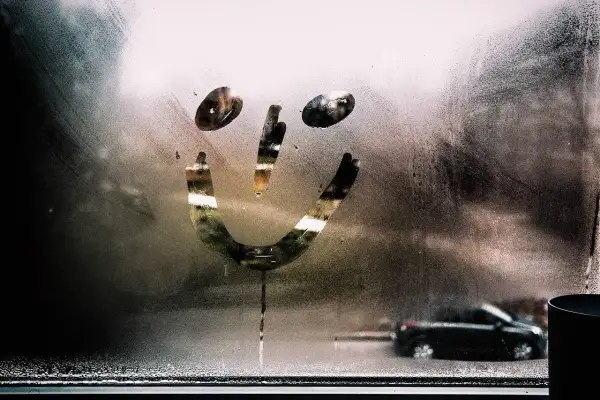 Uśmiechnięta buźka narysowana na zaparowanych szybach w aucie. W tle widać rozmazany czarny samochód.