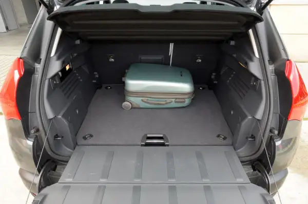 Otwarty bagażnik Peugeot 3008 z jednym zielonym walizką.