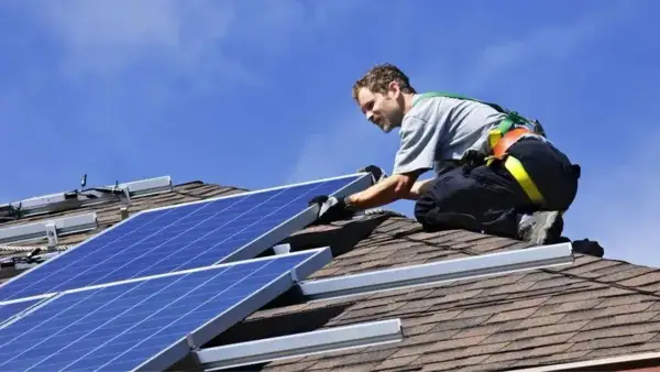Installatore sul tetto, con imbracatura, che fissa pannelli fotovoltaici. L'orientamento dei pannelli è cruciale per massimizzare l'energia solare.