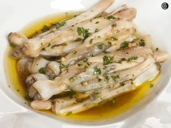 Navajas a la plancha con ajo y perejil, servidas en un plato blanco con aceite dorado.
