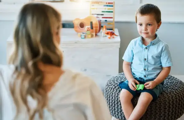 Chłopiec z afazją siedzi na pufie, rozmawiając z terapeutką. Czy dziecku z afazją przysługuje zasiłek pielęgnacyjny?
