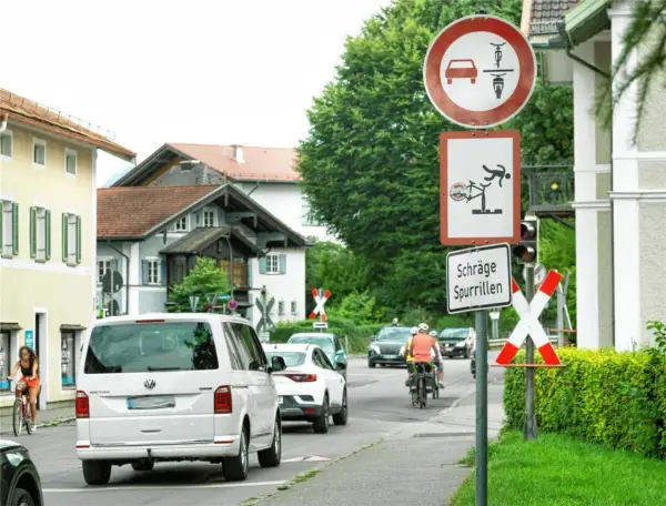 Verkehrszeichen 277 weist auf schräge Spurrillen hin. Ein Radfahrer wird gezeigt, der fast stürzt. Autos und Radfahrer fahren auf einer Straße.