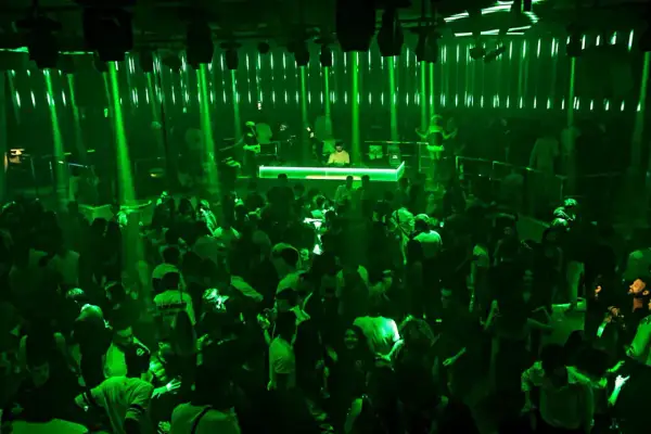 A crowded nightclub with green lights and a DJ booth.