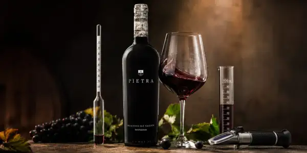 Butelka wina Pietra, kielich z czerwonym winem, winogrona i przyrządy do pomiaru alkoholu. To wino 18 procent, idealne do degustacji.