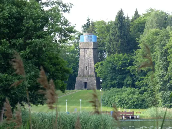 Kamienna wieża Bismarcka w Szczecinku, otoczona zielenią, z błękitnym elementem na szczycie.