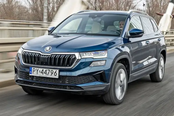 Niebieski Skoda Karoq w ruchu, z kierowcą za kierownicą. Sprawdź aktualną skoda karoq cena.