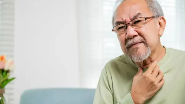 Älterer Mann mit Brille fasst sich an den Hals, deutet auf Probleme beim **Verschlucken im Alter**.