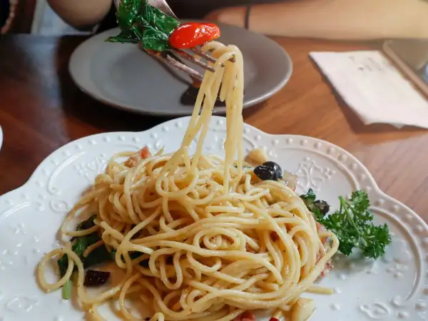 Widok z bliska na talerz pysznego spaghetti aglio olio, z widelcem unoszącym porcję makaronu, listkami bazylii i pomidorkiem.
