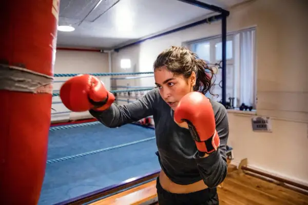 A determined woman in red boxing gloves practices her boxing jabbing technique on a red punching bag in a boxing ring.