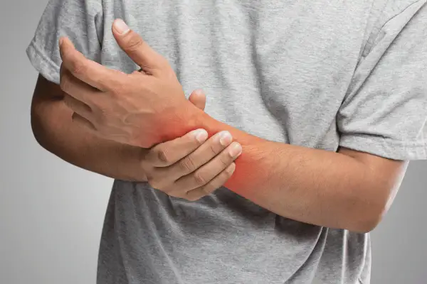 Uomo con dolore al polso, evidenziato da un'area rossa. Potrebbe indicare una distorsione al polso o un'altra infiammazione.