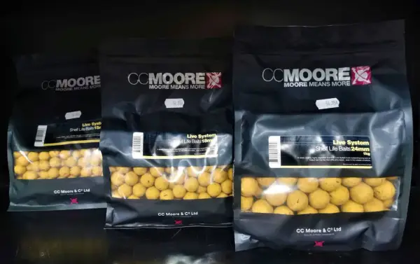 Trzy opakowania kulek proteinowych CC Moore Live System w różnych rozmiarach. Kulki są żółte, widoczne przez przezroczyste okienko.