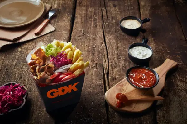 Kebab w pudełku z frytkami, warzywami i sosami na drewnianym stole.