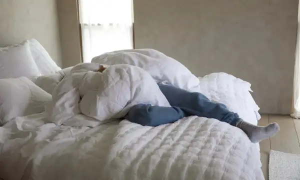 A person sleeps under white linen sheets, a cozy scene that hints at how to wash linen sheets for ultimate comfort.