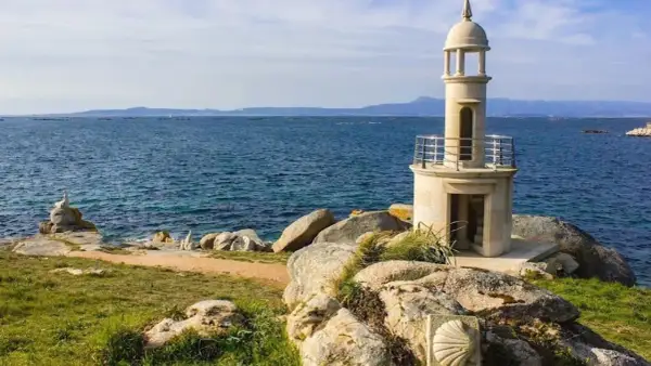 Faro de piedra en Punta Moreiras, con el mar azul de fondo y rocas en primer plano.