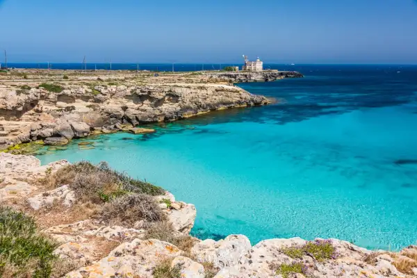 Scogliera rocciosa con mare cristallino e un faro in lontananza, un angolo di paradiso tra le favignana spiagge.