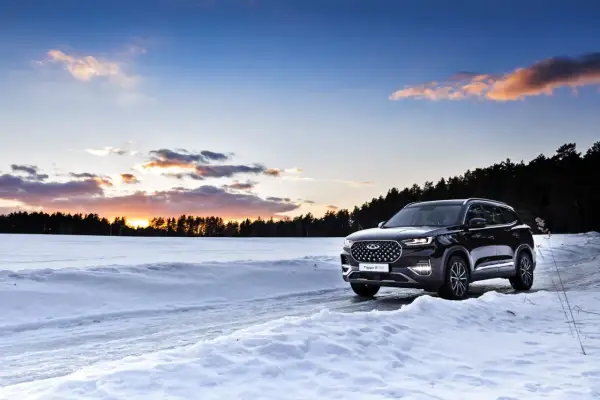 Un SUV noir roule sur une route enneigée au coucher du soleil. La loi montagne impose des équipements pour affronter ces conditions.