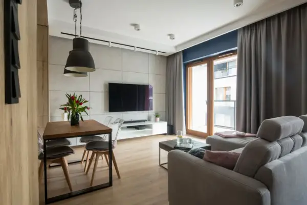 Nowoczesny salon w stylu loftowym z drewnianym stołem, szarym narożnikiem i betonową ścianą.