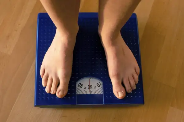 Füße auf einer blauen Waage. Die Anzeige zeigt etwa 80 kg. Muskeln sind schwerer als Fett, aber die Waage zählt beides.