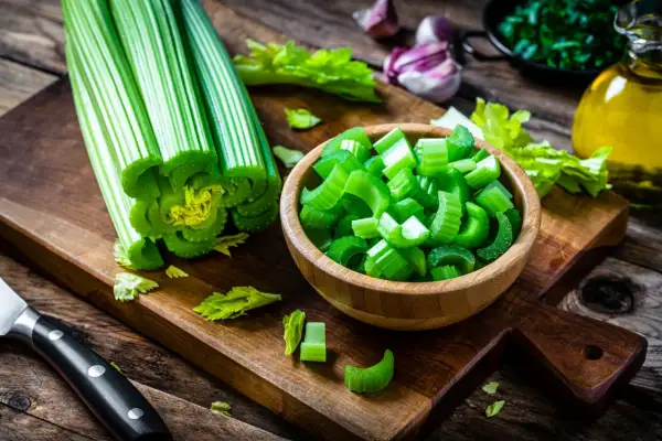 Sedano fresco, tagliato e intero, pronto per essere gustato come verdure che non gonfiano la pancia. Sullo sfondo, aglio, erbe e olio d'oliva.