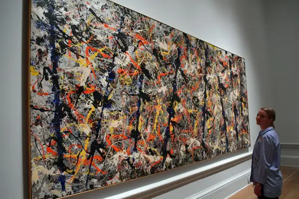 A woman admires a massive Jackson Pollock painting worth $140 million, a chaotic symphony of splattered paint in black, white, orange, and blue.