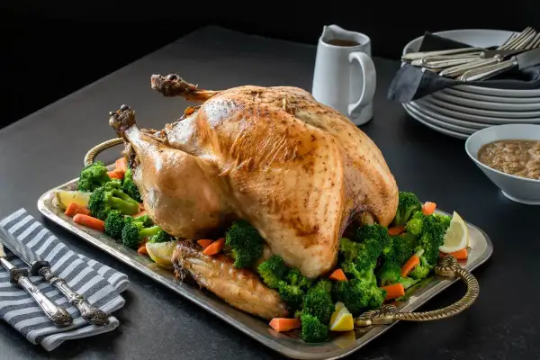 Un jugoso pavo relleno al horno, adornado con brócoli y zanahorias, listo para la celebración.