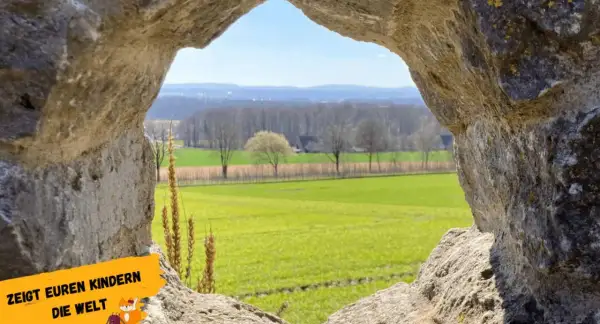 Ein Urlaub am Niederrhein durch ein steinernes Fenster: Grüne Felder, Bäume und ein blauer Himmel.
