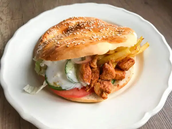 Kebab w bułce z kurczakiem, frytkami, warzywami i sosem na białym talerzu.