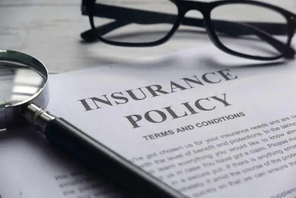 Okulary, lupa i dokument "Insurance Policy" symbolizują analizę polisy PZU po śmierci teścia.