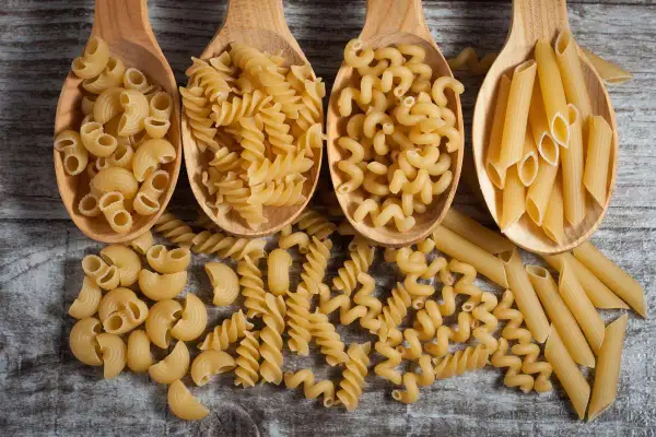 Vier Holzlöffel mit verschiedenen Nudelsorten: Maccheroni, Fusilli, Cavatappi und Penne. Eine Frage, wie viel Gramm Fusilli pro Person?