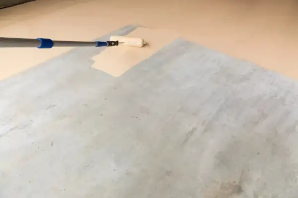 Application d'une peinture claire au rouleau sur un sol en béton, transformant l'espace pour peindre un parquet stratifié.
