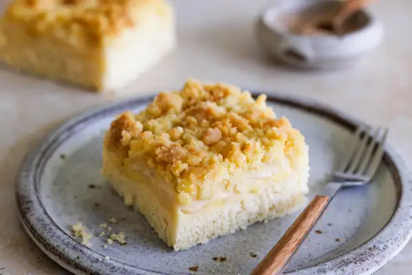 Ein Stück Blechkuchen mit Streuseln auf einem Teller, bereit zum Genießen. Dieses Rezept für Hefeteig Blechkuchen ist ein Klassiker.