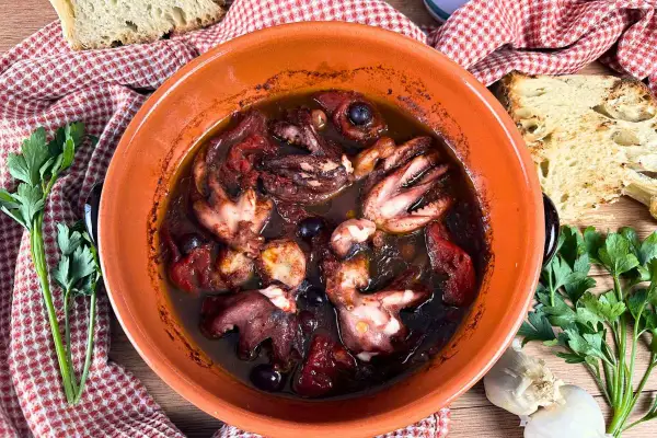 Polipetti alla luciana in terracotta, con pomodoro, olive e pane tostato.