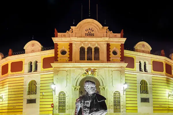 Estatua de un torero frente a la iluminada plaza de toros Almería por la noche.