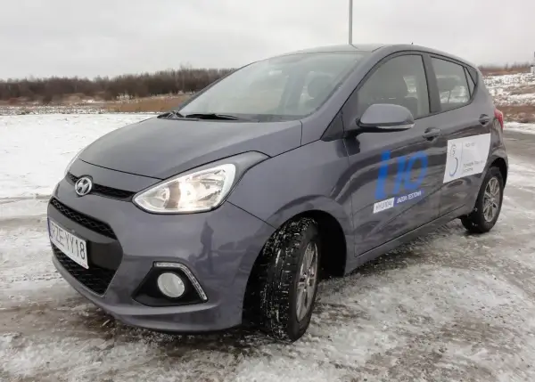 Szary Hyundai i10 na zimowych oponach, gotowy do jazdy testowej po zaśnieżonym terenie.