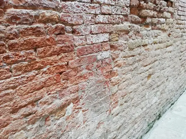 Un muro che sfarina rimedi, con mattoni rossi e bianchi consumati dal tempo, che raccontano storie antiche.