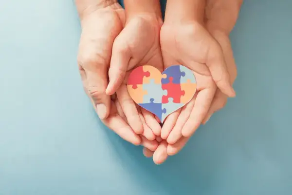 Dłonie trzymają serce z puzzli, symbolizujące wsparcie dla osób z autyzmem i ich unikalne wokalizacje.