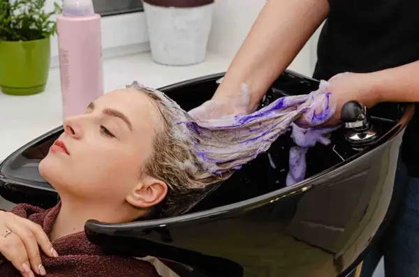 Kobieta w salonie fryzjerskim, jej włosy są myte fioletowym szamponem.