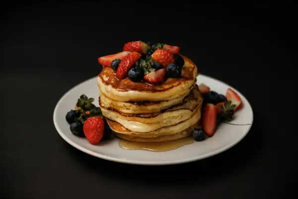 Stos puszystych naleśników z jagodami i truskawkami, polany syropem. Idealny przepis na pancake na weekendowe śniadanie.