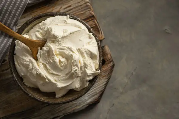 Kremowa masa w misce, idealna jako zamiennik mascarpone. Drewniana łyżka miesza gęsty, biały krem.