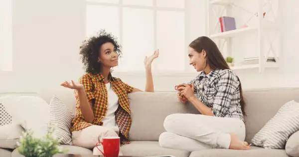 Dwie kobiety siedzą na kanapie, rozmawiając. Jedna z nich gestykuluje, pokazując różne techniki komunikacji interpersonalnej.