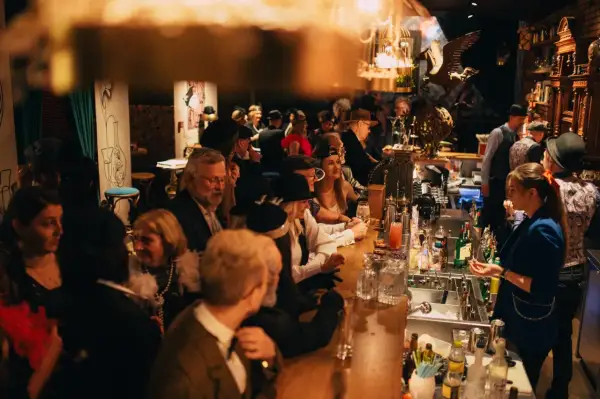 Goście w stylu retro bawią się w restauracji z muzyką na żywo w Warszawie. Przy barze panuje gwar, a atmosfera jest gorąca.