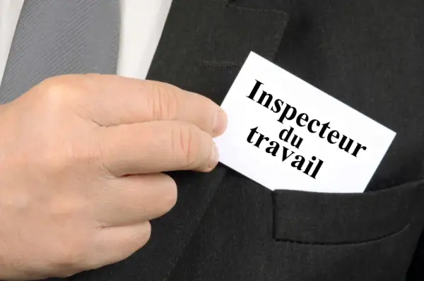 Main d'un homme glissant une carte "Inspecteur du travail" dans la poche d'un costume.