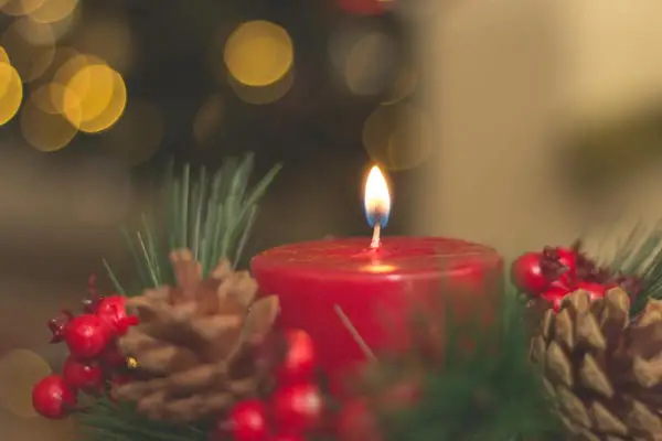 Ein Adventskranz mit brennender Kerze, Tannenzweigen, Zapfen und Beeren. Die Bedeutung des Adventskranzes liegt in der Vorfreude auf Weihnachten.