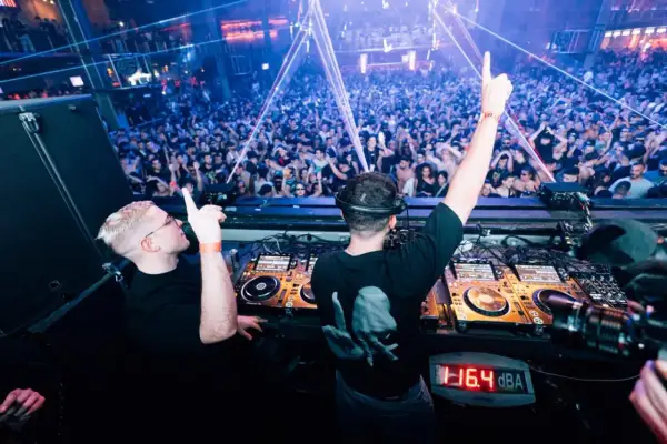 Dos DJs en perfecta alignment, con las manos en alto, animan a una multitud vibrante en una discoteca con luces láser.
